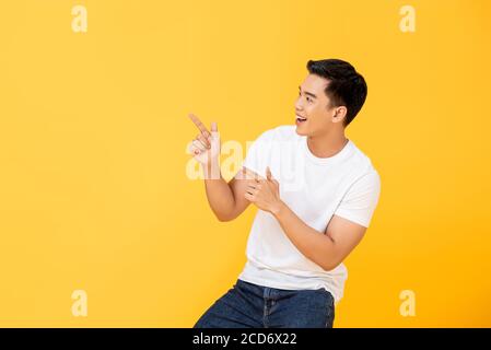 Vista laterale ritratto di sorridente giovane bell'uomo asiatico che punta dita in spazio vuoto da parte in studio isolato sfondo giallo Foto Stock