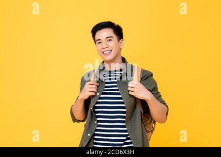 Ritratto di sorridente giovane maschio asiatico turista portare zaino pronto per viaggiare in studio isolato sfondo giallo Foto Stock