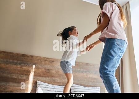 Giovane madre e piccola figlia che si divertono a casa, giocando insieme, saltando a letto, trascorrendo le vacanze insieme, concetto di tempo in famiglia Foto Stock