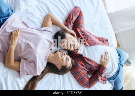 Bei amanti piacevoli che trascorrono il tempo insieme, sdraiati a letto su un foglio bianco, guardando via con i volti felici, bella donna che si allunga la mano fino a toccare Foto Stock