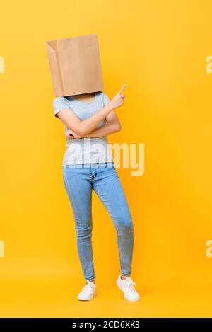 Ritratto concettuale di donna anonima con testa coperta di carta borsa rivolta verso l'alto su sfondo giallo studio Foto Stock