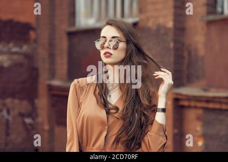 Ritratto di giovane donna con lunghi capelli ricci in occhiali da sole e le cuffie per strada Foto Stock