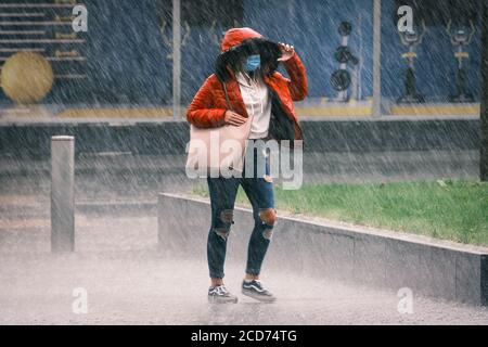 UK Weather: Giovani donne in un cappotto rosso e indossare una maschera facciale è catturato in una doccia a pioggia pesante, Preston, UK Foto Stock