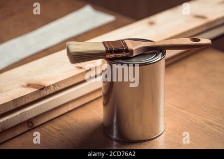 Primo piano di una lattina di metallo con vernice, vernice per legno, che è una nuova spazzola su un tavolo di legno in un'officina Foto Stock