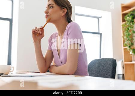 Foto di una bella donna di progettazione mirata che fa schizzi mentre si lavora a tavola in un ufficio luminoso Foto Stock