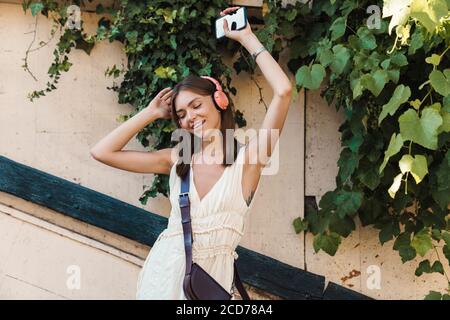 Foto di una bella giovane donna che balla all'aperto mentre ascolti la musica con le cuffie e tieni il telefono cellulare. Foto Stock