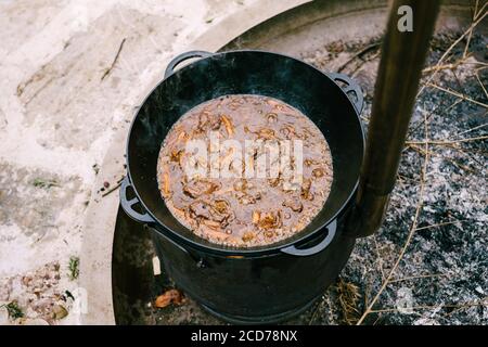 Primo piano di olio bollente e grasso con carne e carote, nel processo di cottura del pilaf uzbeko in un calderone su un fuoco aperto all'esterno. Foto Stock