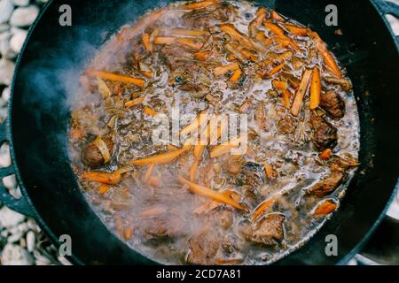 Primo piano della superficie del pilaf finito in un calderone al fuoco. Le grandi carote e la carne di arancio vengono stufate ad alta temperatura. Foto Stock