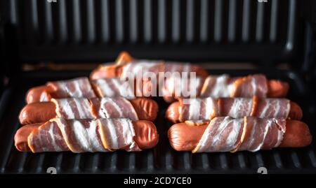 Appetitose salsicce avvolte in pancetta sono grigliate su un elettrico griglia Foto Stock