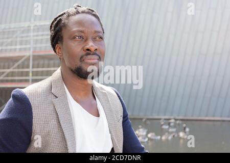 Ritratto dell'uomo africano, capelli lunghi, meditato, giorno d'estate, all'aperto. Foto di alta qualità Foto Stock