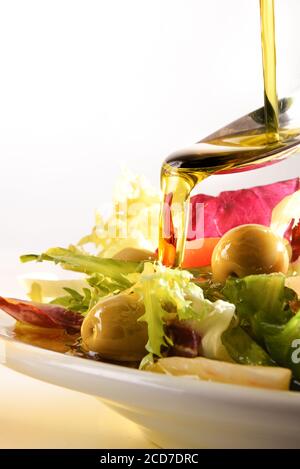 Olio di oliva che cade su cucchiaio condimento insalata primo piano. Composizione verticale. Foto Stock