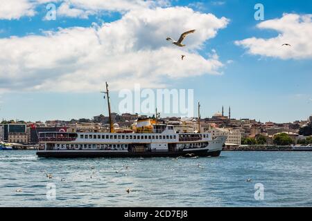 Traghetto che galleggia attraverso il Corno d'Oro, gabbiani che volano nel cielo in una giornata estiva nuvolosa, Istanbul, Turchia Foto Stock