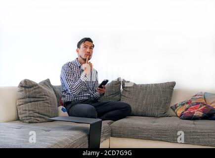 Uomo con smartphone sul divano contemplando opzioni Foto Stock