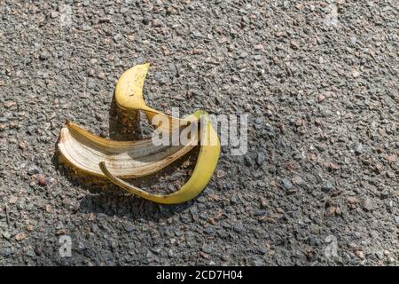 Buccia di banana scartata / buccia di banana sinistra su asfalto footpath / pavimentazione, con leggera ombra dal ramo di albero in testa. Per slip-up, faux pas, blunder. Foto Stock