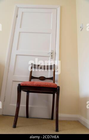 Sedia da pranzo che tiene una porta chiusa in una camera da letto in una casa suburbana, Londra, Inghilterra, Regno Unito Foto Stock