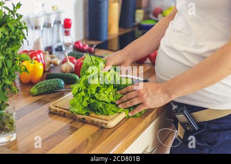 Donna incinta con pompa insulinica che prepara cibo sano nel cucina Foto Stock