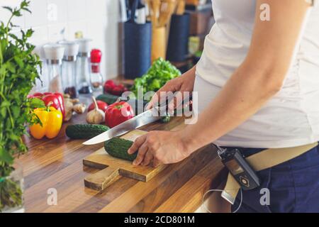 Donna incinta con pompa insulinica che prepara cibo sano nel cucina Foto Stock