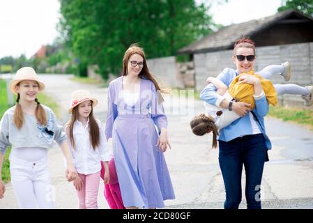 Gruppo di felici famiglie - due sorelle e figlie ragazze camminando lungo la strada della città in una soleggiata giornata estiva Foto Stock
