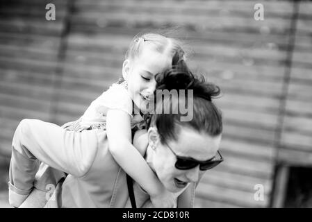 Felice bambina seduta sulle spalle o sulla schiena della madre Foto Stock