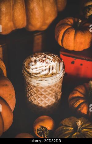 Bevanda di caffè latte con spezie di zucca in un bicchiere alto tra le zucche Foto Stock