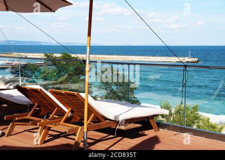 sedie a sdraio vuote sotto un ombrellone sul patio sullo sfondo del mare. Foto Stock