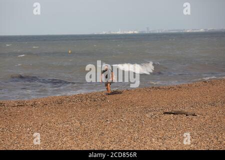 Un uomo cammina lungo la spiaggia e il mare a Brighton, Sussex orientale Foto Stock