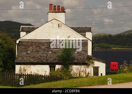 Una casa tradizionale situata tra la fine del canale Crinan a Crinan, Argyll, Scozia e Loch Crinan con una cintura di sicurezza su uno stand nel giardino Foto Stock