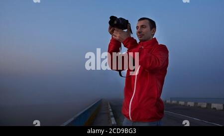 Un uomo su un ponte sul fiume che fotografa un'alba su una nebbia mattina presto. Foto Stock