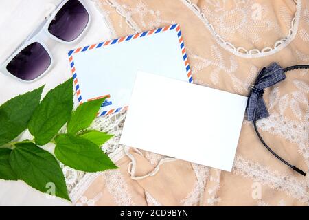 Cartolina nera con busta posta aerea. Sfondo boho con abito in pizzo, archetto e occhiali da sole. Estate vacanza top vista composizione. Postcar su carta bianca Foto Stock