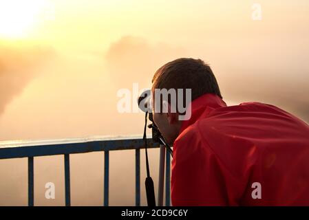 Un uomo su un ponte sul fiume che fotografa un'alba su una nebbia mattina presto. Foto Stock