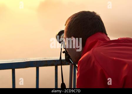 Un uomo su un ponte sul fiume che fotografa un'alba su una nebbia mattina presto. Foto Stock