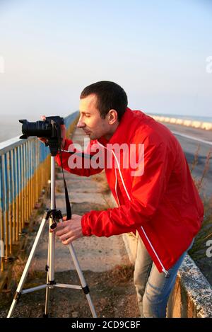 Un uomo su un ponte sul fiume che fotografa un'alba su una nebbia mattina presto. Foto Stock