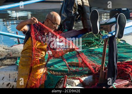 Francia, Corse du Sud, Ajaccio, un pescatore pulisce le sue reti su una delle numerose barche colorate del porto di Tino Rossi, Foto Stock