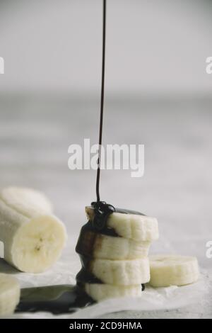 Colpo verticale di fette di banana mentre è versato con sciroppo di cioccolato Foto Stock