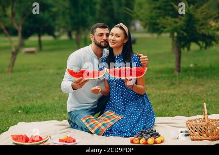 Giovane donna adulta e uomo coppia pic-nic in erba verde prato nel parco divertendosi con l'anguria Foto Stock