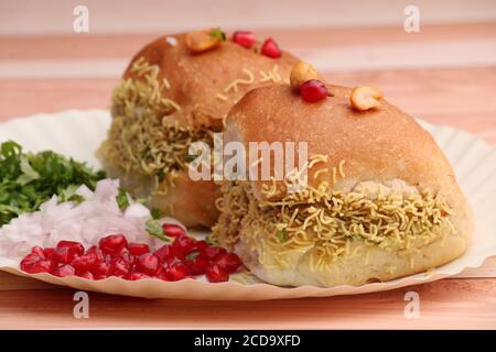 Dabeli è uno snack indiano servito con semi di melograno e Cilantro in piastra di carta bianca. Su sfondo di legno Foto Stock