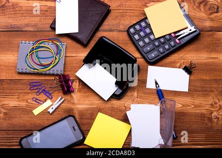 Concetto di idea aziendale. Portafoglio e telefono cellulare su sfondo in legno. Biglietti da visita, leganti, elastici, clip, taccuino, penna e stambolette vicino agli adesivi gialli. Cancelleria, gadget e calcolatrice Foto Stock