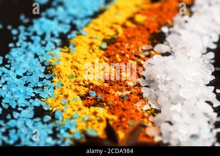Set di spezie su sfondo di legno grigio scuro. Linee di colori arancio, blu, bianco e giallo, fatte di sale marino granulato, paprica e spezie turmeriche. Concetto di arte alimentare. Composizione di condimento colorato Foto Stock