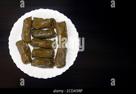 Foglie di vite ripiene su piastra bianca su sfondo di legno scuro con spazio per la copia. Famosa cucina tradizionale mediorientale, turca, asiatica. Dolma o farcito Foto Stock