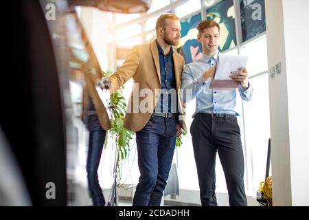 giovane venditore di automobili caucasiche mostrano la migliore variante al cliente in concessionaria. bell'uomo d'affari è venuto per ottenere nuovo auto. consulente aiutarlo con ch Foto Stock