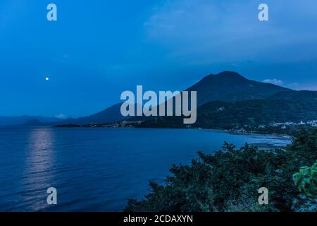 La luna piena che sorge sul lago Atitlan in Guatemala. In primo piano è la città di San Juan la Laguna. Le doppie cime del vulcano Toliman sono a. Foto Stock