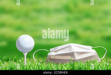 Golf ball on tee e maschera medica viso sul campo durante COVID-19 coronavirus Concept con sfondo bokeh sfocato e spazio di copia. Foto Stock