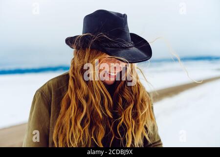 Donna occidentale fiduciosa con cappello cowboy cammina intorno alla neve con la sua macchina fotografica e capelli che scorre nel vento. Foto Stock