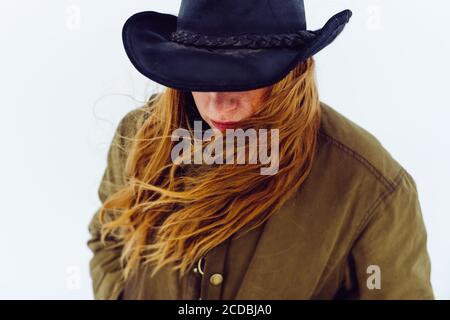 Donna occidentale fiduciosa con cappello cowboy cammina intorno alla neve con la sua macchina fotografica e capelli che scorre nel vento. Foto Stock