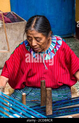 Una donna maya Cakchiquel più anziana in abito tradizionale avvolge il filo su un telaio per prepararsi a tessere su un telaio posteriore a Santa Cruz la Laguna, Guatemala. Foto Stock