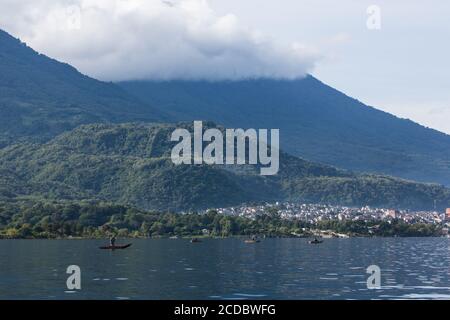 Gli uomini maya a cayucos pescano nel lago Atitlan con la città di Santiago Atitilan, Guatemala, con il vulcano Atitlan alle spalle coperto di nuvole Foto Stock