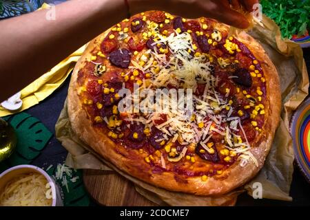 La pizza fatta in casa appena sfornata viene cosparsa di formaggio Foto Stock