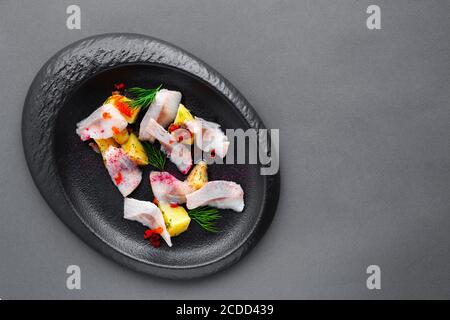 Antipasto freddo aringhe salate con patate bollite su piatto nero Foto Stock