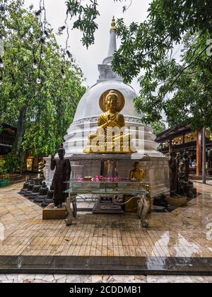 Colombo, Sri Lanka - 25 novembre 2019: Statua di Buddha sullo sfondo dello Stupa Bianco in tempo piovoso al Tempio di Gangaramaya a Colombo, Sri Foto Stock