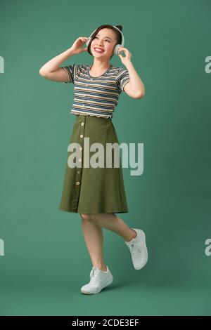 Beautiful young woman in headphones listening to music and dancing on green background Stock Photo